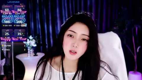 Media: Video of an Asian woman with long black hair, fair skin, wearing a white blouse, in a dimly lit room with a \"2015\" countdown screen and \"Happy New Year\" text in the background.