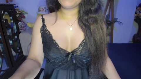 Media: A video of a woman with long, wavy brown hair in a black lace nightgown, her cleavage visible, in a dimly lit room with bookshelves and a blue carpet.