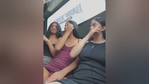 Media: Video of three young women with light brown skin, wearing revealing outfits, sitting in a car, smiling and looking at the camera.