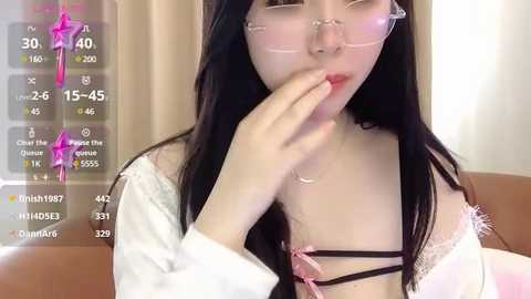 Media: Video of an East Asian woman with long black hair, wearing glasses, a pink bra, and a white off-shoulder top, seductively biting her finger, set in a modern, indoor environment.