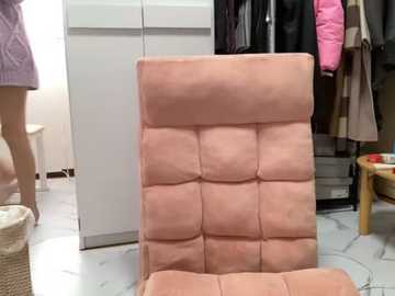 Media: Video of a person in a lavender robe standing beside a plush, light pink, tufted leather chair with a white marble floor and a closet filled with jackets.