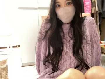 Media: Video of a young Asian woman with long black hair, wearing a light purple knit sweater, face mask, and sitting on a white bed. Background includes white wardrobe and a wicker basket.