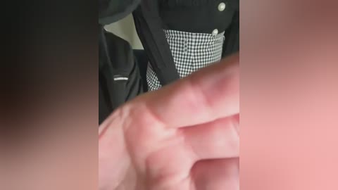 Media: A video shows a close-up of a person's hand, with fingers spread, partially obscuring a black and white checkered dress. The background includes a black jacket and a blurred, indistinct setting.