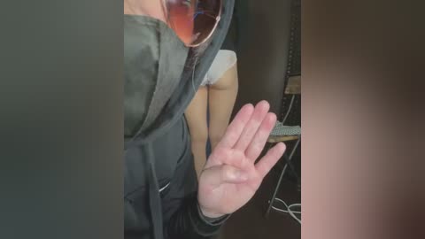 Media: Video of a person with light skin and a large nose, wearing glasses, a green hoodie, and white underwear, sitting on a dark wooden table.