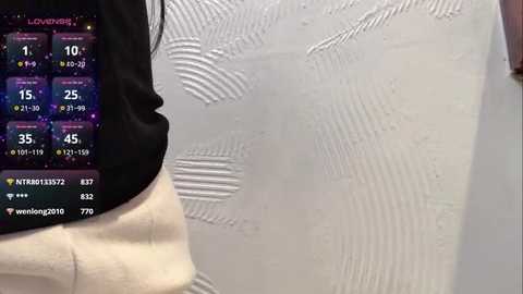 Media: Video of a person's arm and hand in a light-colored sleeve, holding a smartphone displaying a weather app with temperature and precipitation forecasts. The background features a textured, light-colored wall with faint waves.