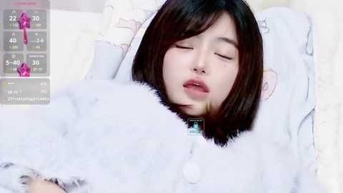 Media: Video of an Asian woman with straight, dark hair, lying asleep in a white, fluffy blanket. Her eyes are closed, and she has a peaceful expression.