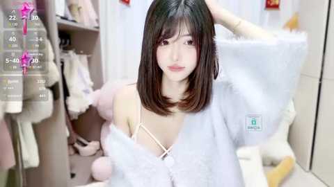 Media: A video of a young Asian woman with shoulder-length black hair, wearing a white off-shoulder dress, sitting on a bed in a bright room.