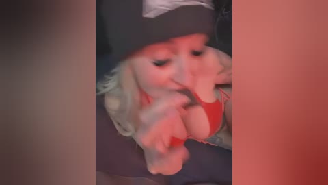 Media: Video of a young woman with fair skin, wearing a black beanie and red top, leaning forward, appearing to be in a car.