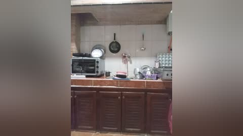 Media: A video of a rustic kitchen with a wood-burning stove, an oven, and cabinets; a metal rack holds cooking utensils; a window with a circular design is visible; the walls are tiled with a light color.