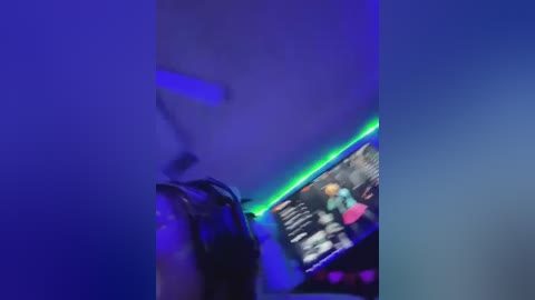 Media: A blurry video of a dimly lit room with a person wearing headphones, likely gaming, with a neon blue LED strip lighting the scene.