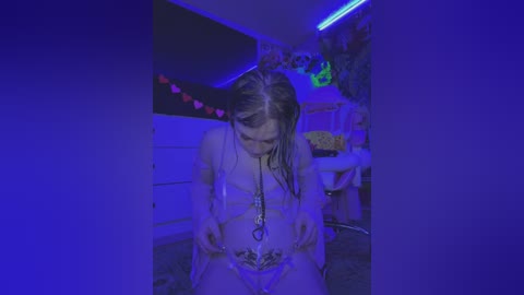 Media: Video of a woman with wet, dark hair kneeling in a dimly lit, neon-lit room with a bed, dresser, and floral wallpaper in the background.