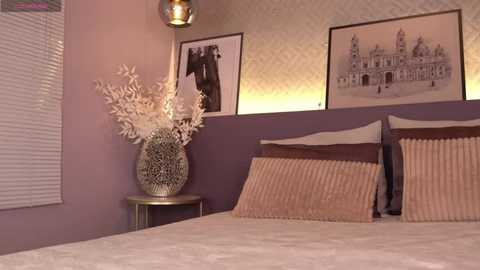 Media: A video of a modern bedroom with lavender walls, a bed adorned with beige pillows, a wooden headboard, and a decorative vase. Two framed black-and-white prints hang above.