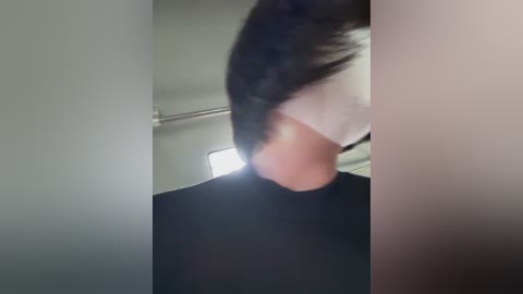 Media: A blurred video of a person with long black hair, wearing a white mask, standing in a dimly lit bathroom with a metallic shower rod visible in the background.