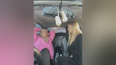 Media: Video of two blonde women in a car, one wearing a bright pink sweater and the other a black sweater, engaging in conversation.