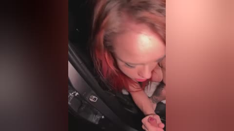 Media: Video of a woman with long, dyed red hair, wearing a black top, leaning into a car window, her eyes closed, suggesting a moment of intimacy or relaxation.