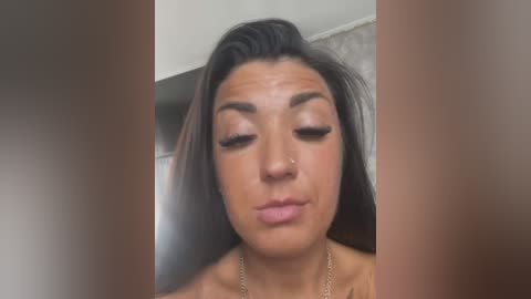 Media: Video of a woman with long, dark hair and tan skin, wearing a nose stud, making a kissy face, blurred background, brownish vertical edges.