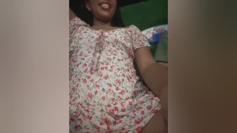 Media: Video of a smiling woman in a floral dress, lying on a green couch, with blurred background.