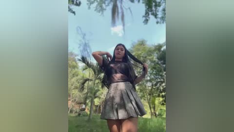 Media: Video of a Latina woman with long dark hair, wearing a black sheer top and checkered skirt, posing in a lush, green park with tall palm trees and a clear blue sky.