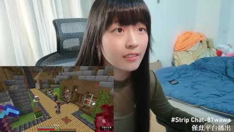 Media: Video of a young Asian woman with straight black hair and fair skin, wearing a green top, gazing at a Minecraft screen on a computer. The background shows a messy bedroom with a blue bed and a black chair.