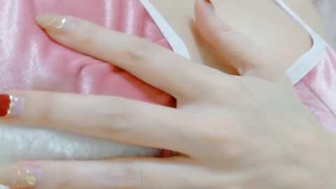 Media: Video of a pale hand with manicured nails featuring gold glitter polish, resting on a soft, pink satin surface. The background includes a blurred, light-colored pillow.