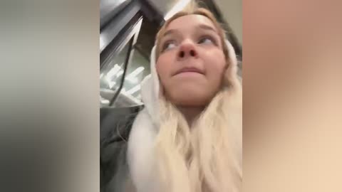 Media: Video of a young woman with blonde hair and fair skin, looking contemplative in a car. She has a neutral expression and wears a light-colored hoodie. The car's interior is visible in the background.