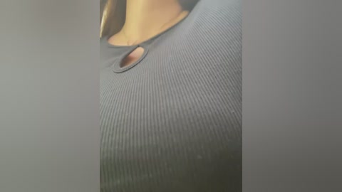 Media: Close-up video of a person wearing a ribbed, grey t-shirt with a small hole in the chest area, revealing a slight glimpse of a light skin tone.