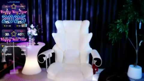 Media: Video of a luxurious, white, swivel chair with a high backrest, set against dark, vertical curtains. Background includes a table with a vase of white flowers and a digital display showing \"Happy New Year 2025.\