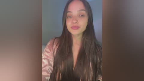 Media: Video of a young woman with long, straight black hair, fair skin, and light pink lipstick. She wears a shiny, pale pink satin robe, against a blurred, softly lit background.