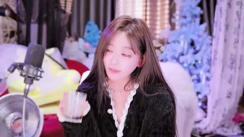 Media: Video of a young Asian woman with straight brown hair, wearing a black cardigan, holding a glass, in a cozy, softly lit room with Christmas decorations.