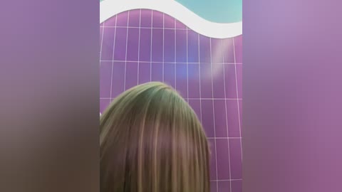 Media: A video of a person with straight, light brown hair, facing a tiled wall with a wavy pattern in purple and white. The image is slightly blurred, emphasizing the abstract, dreamlike quality.