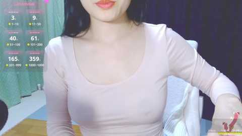 Media: Video of an East Asian woman with fair skin, wearing a light pink, long-sleeved top, revealing small breasts. She has long black hair and is sitting on a bed.