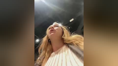 Media: A video of a blonde woman with light skin, wearing a white, ribbed sweater, captured from a low angle, with sunlight streaming in, creating a halo effect.