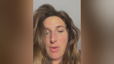 Media: Video of a young woman with wavy, shoulder-length brown hair, closed eyes, and slightly parted lips, blurred background.