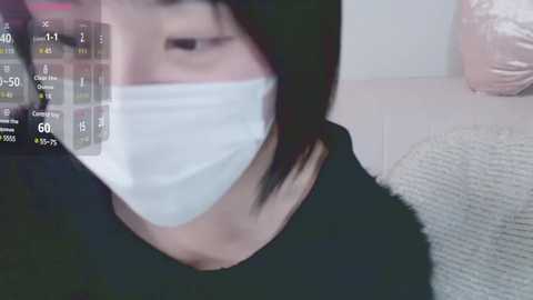 Media: A video shows a person wearing a white surgical mask over their mouth, with a digital overlay displaying health metrics on their face. The background includes a gray couch and a white wall.