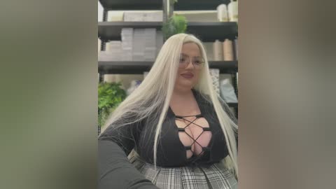 Media: Video of a curvy, blonde woman with long hair, wearing a black lace-up top and a plaid skirt, standing in a well-lit room with shelves full of books and plants in the background.