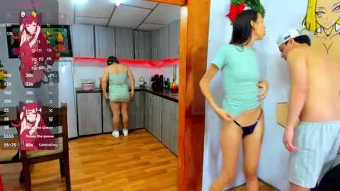 Media: A video of a kitchen and a man and woman in a living room. The woman, wearing a green shirt and black thong, stands in front of a wall; the man, shirtless, wears a hat and shorts, looking at her.