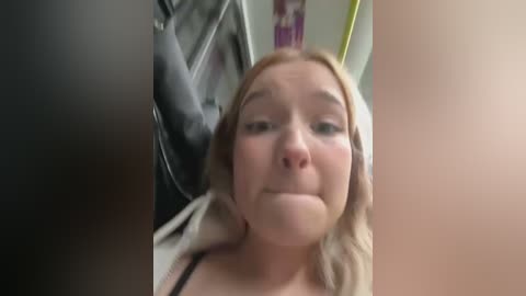 Media: A blurred video of a Caucasian woman with fair skin and blonde hair, wearing a black bra, sitting in a laundry room with a white washing machine in the background.