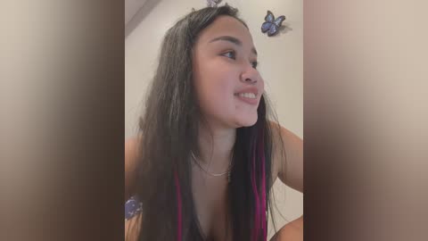 Media: Video of a smiling young woman with long, straight black hair and pink streaks, wearing a sleeveless top, in a room with butterflies on the wall.