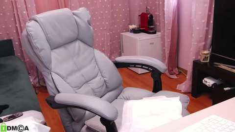 Media: Video of a pink-patterned office with a light blue leather chair, a computer, and a red kettle on a white cabinet.