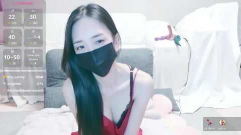 Media: A video of an Asian woman with long black hair, wearing a red lace bra and black mask, kneeling on a bed with a white sheet and a pink blanket.