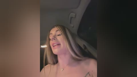 Media: A video captures a smiling, fair-skinned woman with long blonde hair, wearing a strapless top, in a dimly lit car interior.