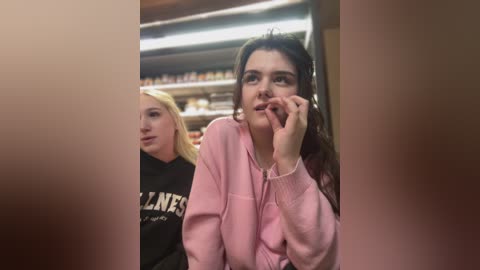 Media: Video of two young women, one with long dark hair and a pink hoodie, the other with blonde hair and a black hoodie, in a dimly lit convenience store.