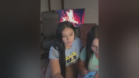 Media: Video of a young Asian woman with long black hair, wearing a SpongeBob t-shirt, sitting on a couch in a dimly lit living room, watching a TV with a fire screen.