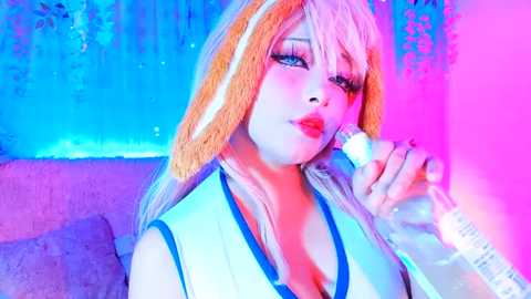 Media: Video of a young woman with blonde hair, wearing bunny ears, and red lipstick, holding a bottle, in a colorful, neon-lit room.