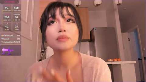 Media: A video of an Asian woman with fair skin, dark hair, and light makeup in a modern kitchen, with a digital overlay displaying health metrics.