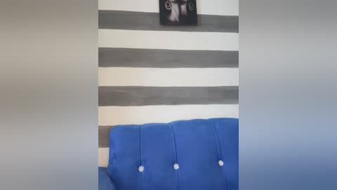 Media: Video of a modern, minimalist room featuring a blue tufted couch with three white buttons against a wall with horizontal gray and white stripes.