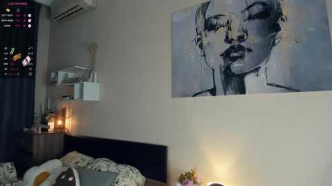 Media: Video of a modern bedroom with a black-and-white abstract art print of a woman's face on the wall, a bed with floral-patterned sheets, a nightstand with a lamp, and an air conditioner.