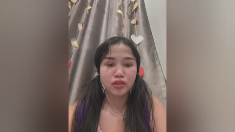 Media: Video of an East Asian woman with long black hair in pigtails, wearing a purple top, in a shower stall with heart-patterned shower curtain.