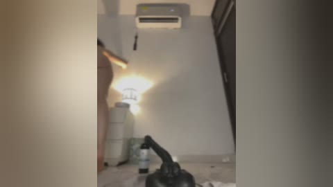 Media: A video of a narrow, dimly lit hallway with beige walls and a central air conditioner. A black vacuum cleaner is in the foreground, and there are several white storage containers along the wall. The scene appears to be in a residential setting.