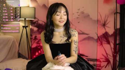 Media: A video of an Asian woman with long black hair, wearing a black velvet dress, holding a pink feather duster, in a pink-lit room with a digital clock and a black lamp.